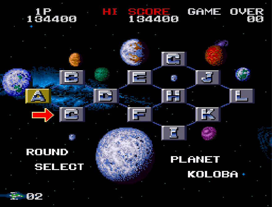 The stage select screen for Darius Twin (SNES), a view of the stars with a galaxy resembling the Milky Way in the background. There is a grid of squares lettered from A to L, with a planet next to each square to represent the stage. The squares are all a gray background except for A, which is gold, since it has been completed. There is an arrow pointing at C, and the bottom of the screen reads "ROUND SELECT" on the left and "PLANET KOLOBA" on the right. There is a score readout at the top of the screen and a lives counter in the bottom left.